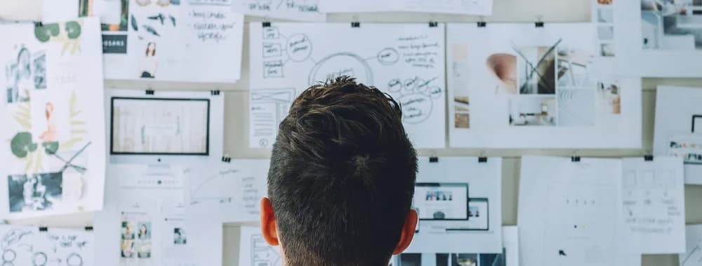 A strategist in front of a wall of printed wireframes, sitemaps and notes, working out which direction to take.